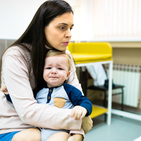 The baby is crying at the doctor’s, sitting on woman’s lap.