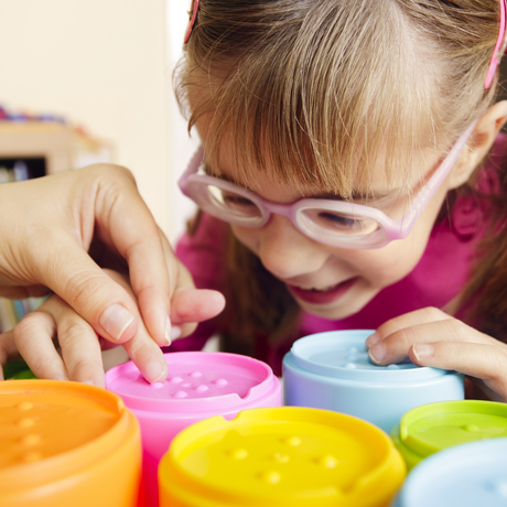 Girl with poor vision playing with colourful tactile toy cups as a part of occupational therapy.